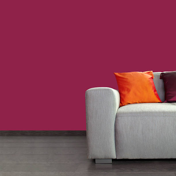 Modern gray sofa and colorful pillows against purple wall