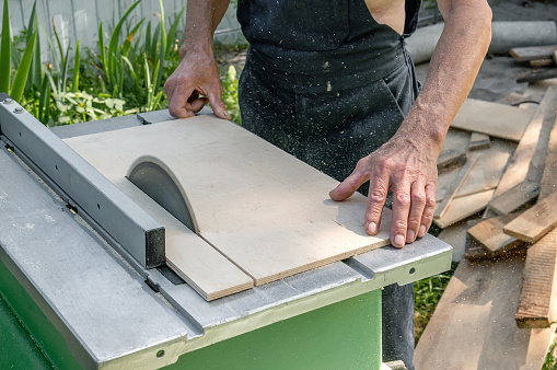 turner works on a lathe. Close-up. saw table. a man saws a tree with a milling machine. An experienced carpenter cuts a wooden board with a circular saw. Production of wood materials. Real life.