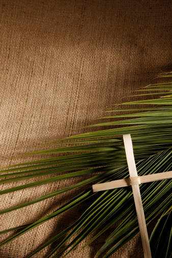 Palm Sunday Holiday. Wooden cross with palm leaf on light background with copy space. Religion background suitable for faith religion, christian holidays, Easter, Redeemer, the Feast of Corpus Christi