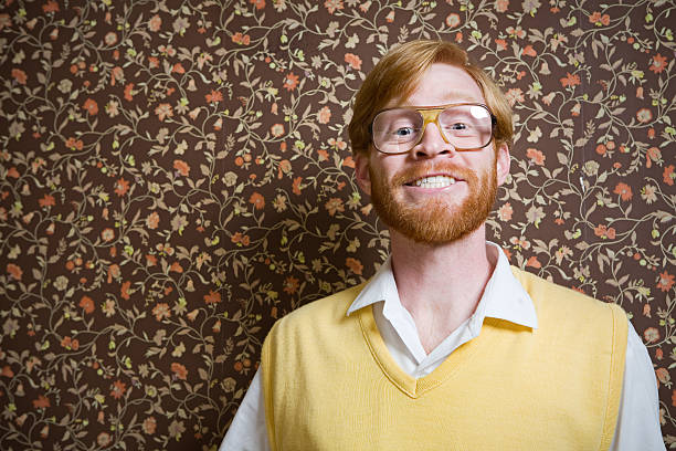 A man in 1960's-1970's style stands in his floral vintage wallpaper living room smiles for a portrait. Horizontal with copy space.