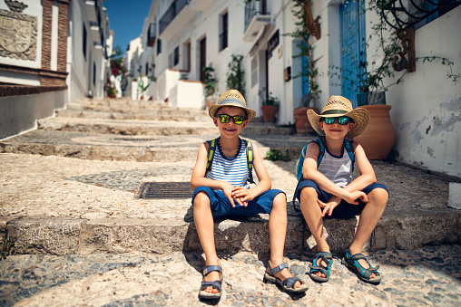 Two little boys sightseeing a town in Andalusia, Spain\nBoys are sitting on cobblestone street and resting.\nShot with Nikon D810