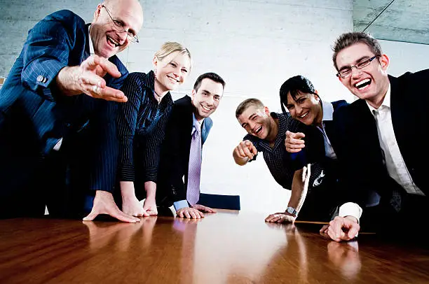 Group of mischievous business people laughing and sneering at camera / at the spectator