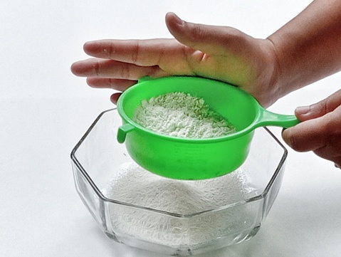 Sifting flour into a glass bowl.