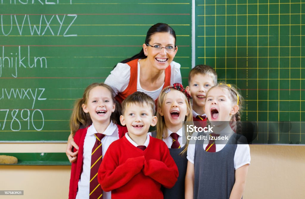 School Kids Posing With Their Teacher, Portrait Five school kids standing together with their teacher, shouting and laughing, singing. Green Color Stock Photo