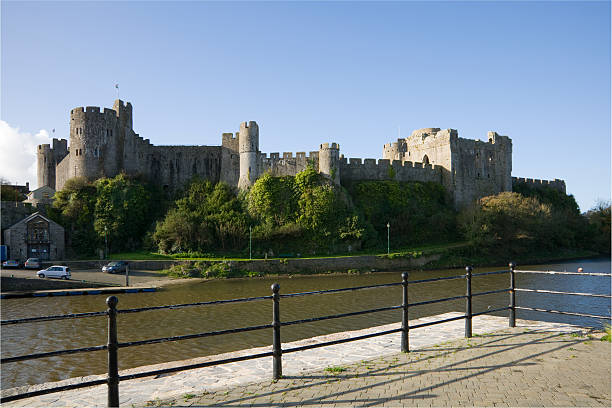 Pembroke, Wales - 02 28 2023: old medieval Pembroke castle on a green hill top surrounded by buildings with water below