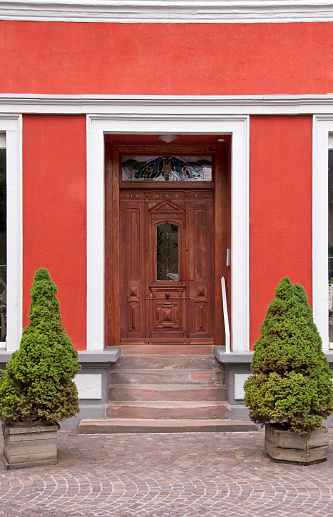 Red and white colored house with ornamented door. Two green pot plants are standing beside the stairs. Entrance to a retail store.  Vertical orientation.