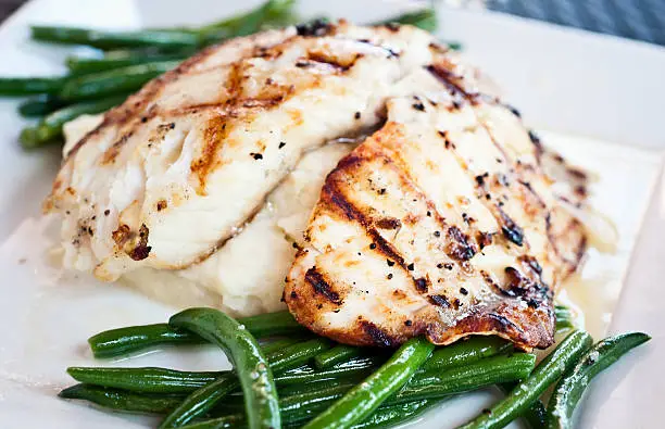 char grilled fillet of fish over mashed potatoes and green beans close up