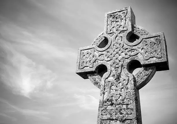 A low angled view of an old and weathered Celtic cross with plenty of space for copy and text.