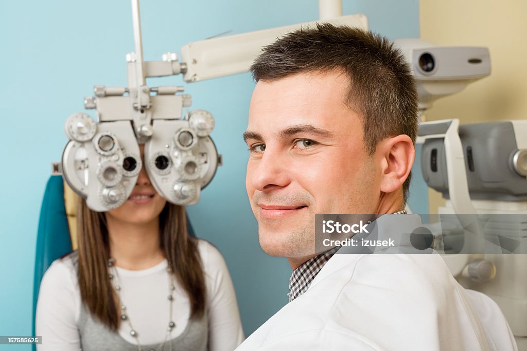 Optometrist Eye Exam Tonometer Optometrist looks at camera while examining the eyes of a young woman patient with a tonometer. Doctor Stock Photo