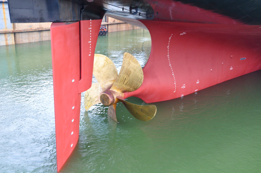 A view of the rudder and propeller of a ship. The ship is undergoing repair work at a dry dock.