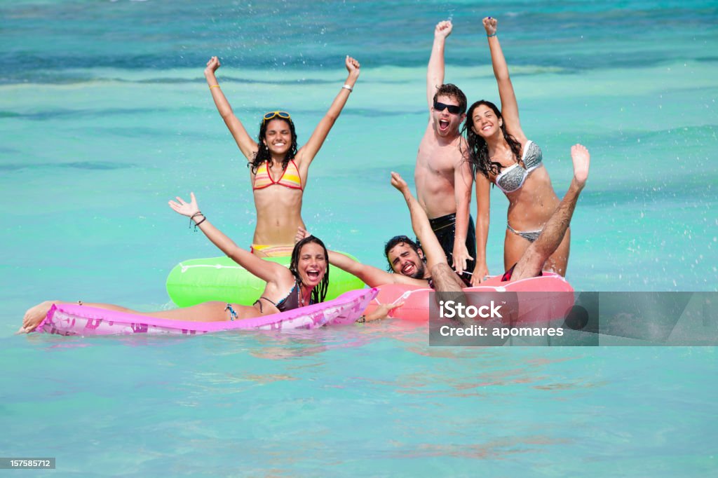 Grupo de jovens com boias flutuando em uma praia - Foto de stock de Adolescente royalty-free