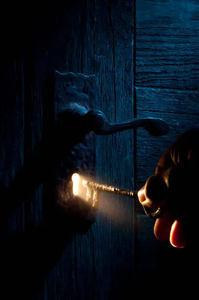 Mysterious door exterior under blue light with a golden ray of light emanating from the keyhole from the other side, lighting a skeleton key being held by an unknown stranger.http://www.garyalvis.com/images/conceptsIdeas.jpg