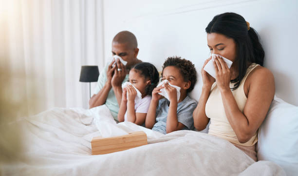 malade, grippe et famille sur un lit, mouchoir en papier et nez en proie à la maladie, maladie et rhume à la maison. parents, mère et père avec frères et sœurs, enfants et enfants dans une chambre à coucher, allergie et problème de santé - domestic life sadness family bed photos et images de collection