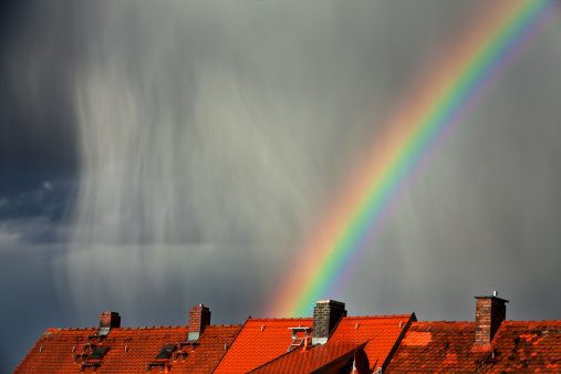 It is raining in the last evening sun. Over roofs in front of the dark sky a rainbow is shining. Canon 5D Mark II and tele with ISO 100.