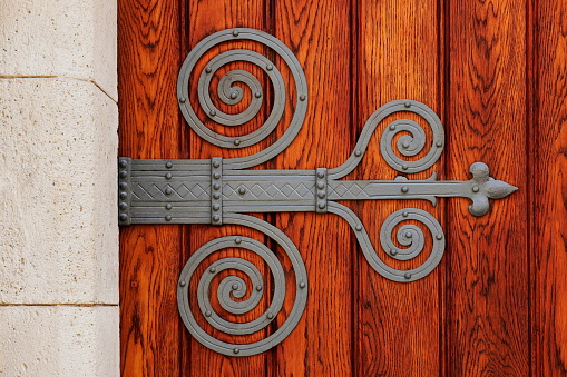 decorative forged mounted wrought iron vintage steel hinge on stained oak gate. closeup door detail. architecture, travel and tourism concept.