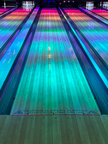 Stock photo showing close-up view of ten pin bowling lane with multicoloured lighting and pinsetter returning bowling pins back in their original positions.