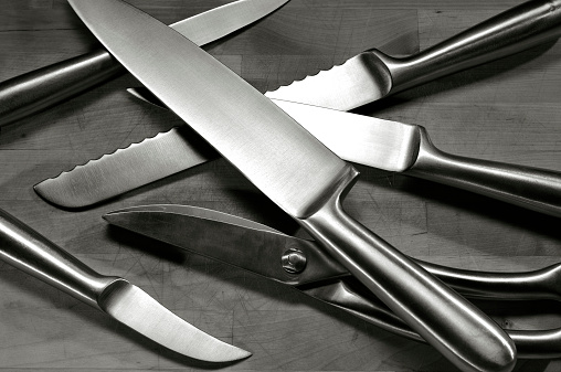 Set of stainless steel blades arranged on a wooden cutting board. Warm black and white shot.