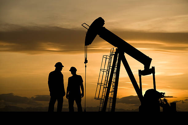 Oil Industry Workers Meeting Two oil and gas workers hold a meeting in front of a pumpjack against a yellow dawn sky. oil pump petroleum equipment development stock pictures, royalty-free photos & images