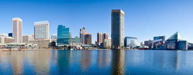 Panorama of Baltimore's Inner Harbor with numerous skyscrapers casting a reflection in the early morning sunshine.
