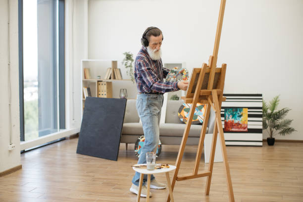 istock Aged artist in headphones working with paint in studio space 1575889685