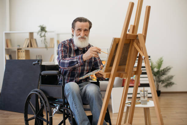 istock Happy retired man on wheelchair posing on camera with brush 1575890237