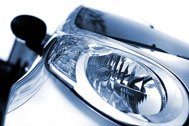 Headlight of a new car on Close up of the head lights of a new car. The color of the car is silver metallic, blue. The background is white. Front view, left wing. photographed with a 50mm prime lens and full frame camera.modern car-light, isolated on white, toned image bmw dealership stock pictures, royalty-free photos & images