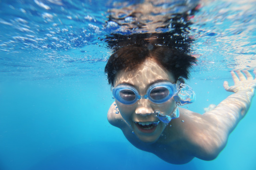 Asian boy swimming underwater. Shallow DOF with focus on foreground bubbles.