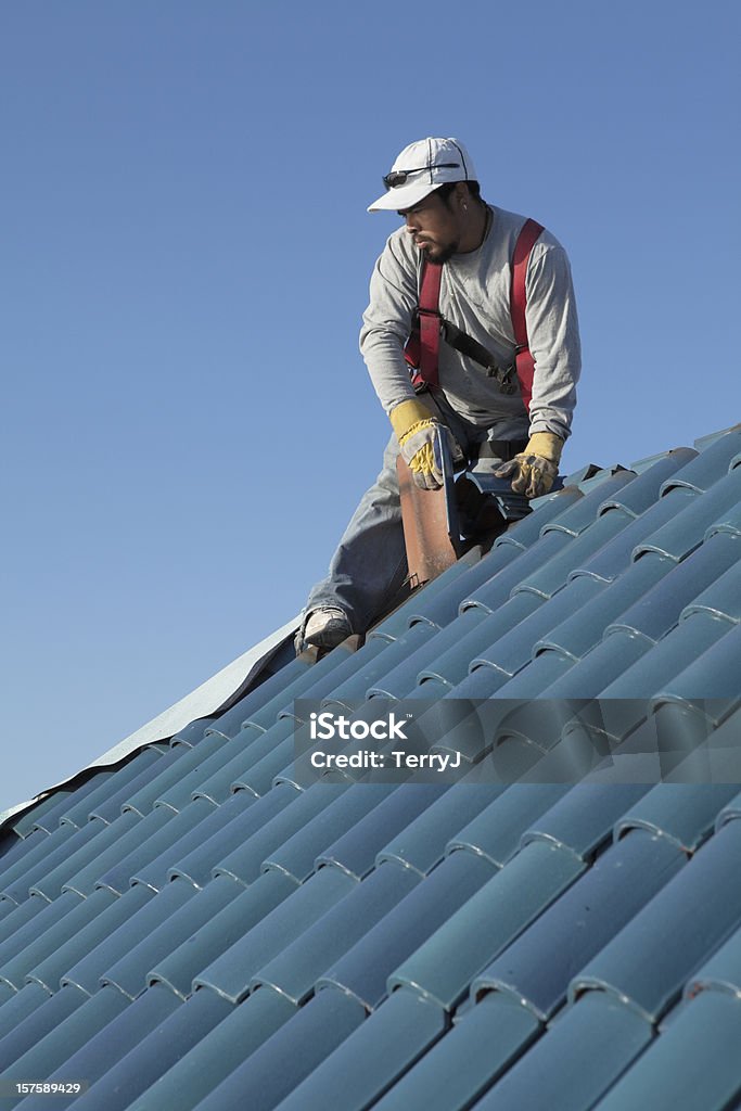 Dirty Jobs Hispanic roofer taking the roof tile off to start a reroof. Roofer Stock Photo