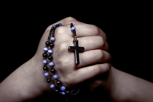A rosary is held by female hands.