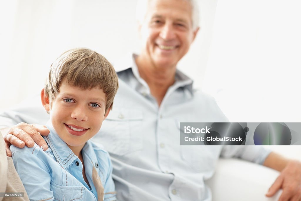 Jovem garoto sorridente sentado com seu avô em segundo plano - Foto de stock de 10-11 Anos royalty-free