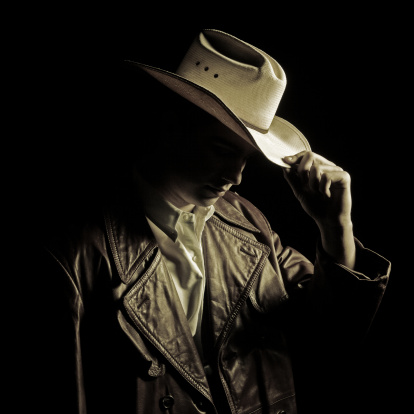 mysterious young cowboy wearing a leather long jacket and cowboy tipping is hat
