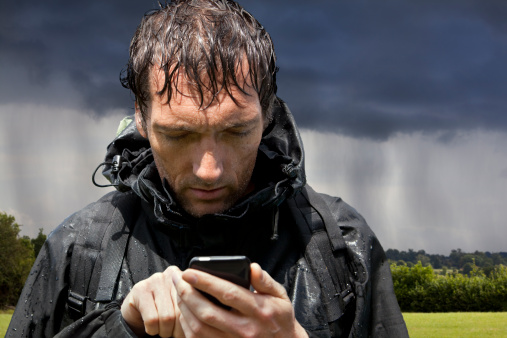 Backpacking hiker soaked by passing rainstorm looking at touchscreen GPS smartphone, for sat nav map app directions or looking at emails etc.