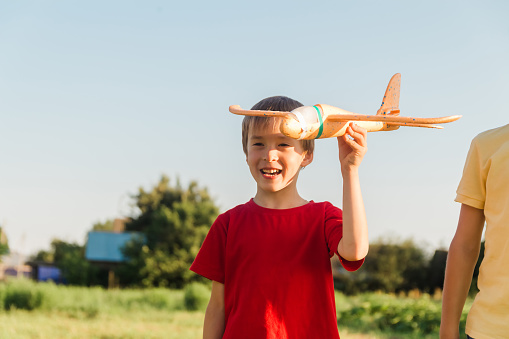 Two boys runs with toy airplane in summer through field. Happy children running around in park, playing with toy airplane outdoors. Brothers dreams of flying. Carefree kids playing. Happy family.