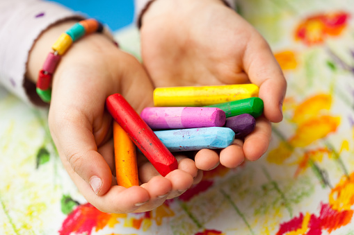 Hands of a child holding wax crayons. Drawing in the background. Soft focus.\n\n[url=/file_closeup.php?id=12638403][img]/file_thumbview_approve.php?size=1&id=12638403[/img][/url]