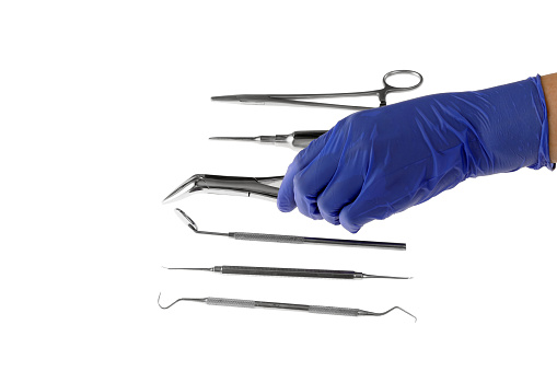 Dentist's hand in a rubber glove with a rubber dam clamp forceps and a clamp with a dental clinic on the background. Medical tools concept.