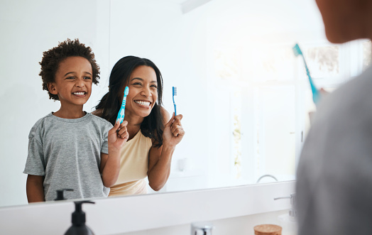Teaching, mama and son brushing teeth, wellness and cleaning mouth at home, bathroom and smile. Family, female parent and mother with male child, kid and boy with reflection, health or dental hygiene