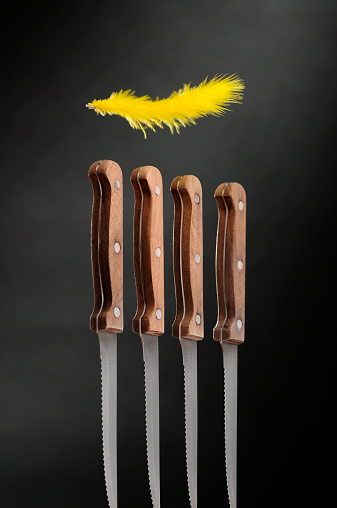 Flying yellow feather over the knives. Four stainless steel knives with wooden hand arranged in a row.