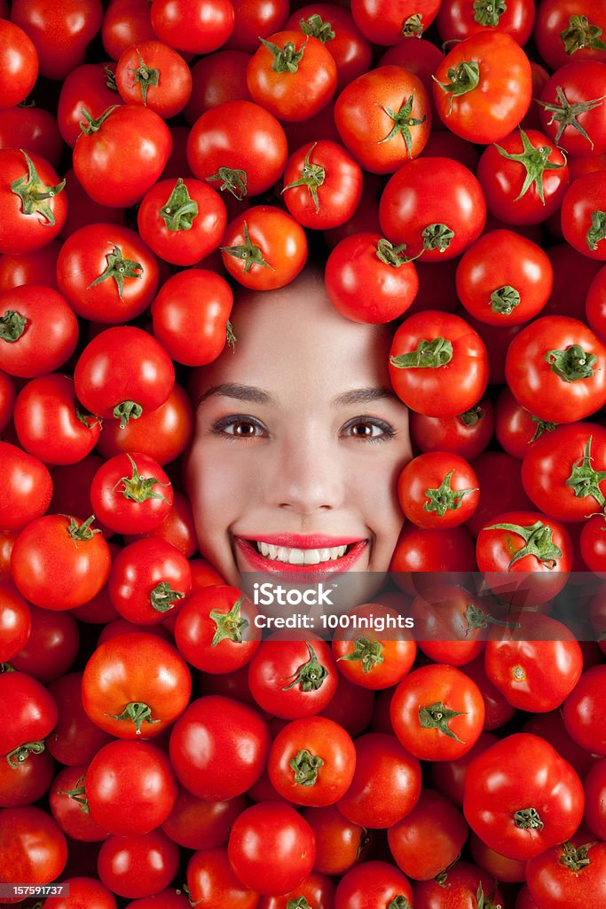 Tomato Girl Face of beautiful young woman among red fresh tomatoes. Adult Stock Photo