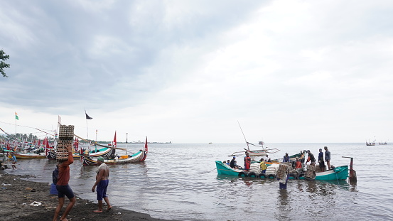 fishermen and traders as well as local residents at East java Indonesia carrying basic food groceries needs from traditional wooden boats. sea ​​transportation of foodstuffs such as egg and rice