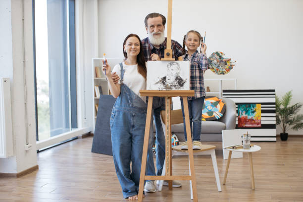 mother, daughter and granddad posing near easel and smiling - group of people art museum clothing lifestyles imagens e fotografias de stock