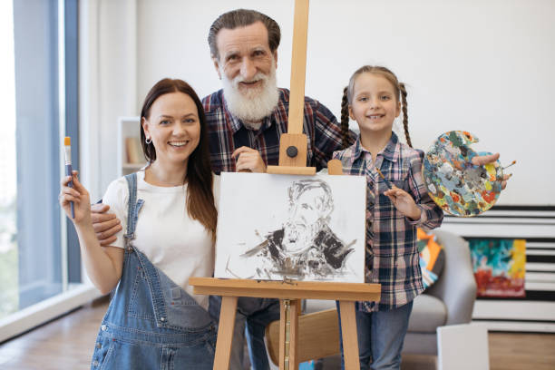 madre, hija y abuelo posando cerca del caballete y sonriendo - group of people art museum clothing lifestyles fotografías e imágenes de stock