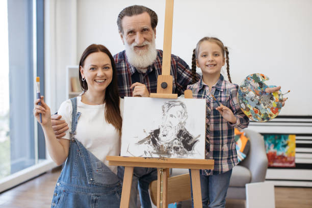 mother, daughter and granddad posing near easel and smiling - group of people art museum clothing lifestyles imagens e fotografias de stock