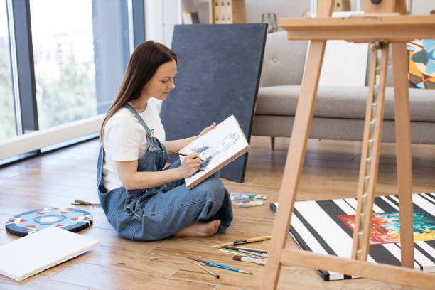 istock Talented lady drawing portrait of man while sitting on floor 1575919510