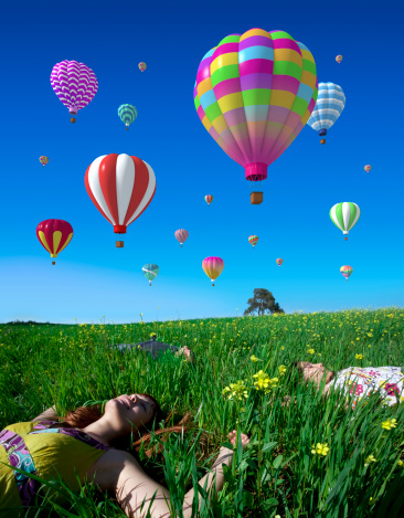 A young woman with two children lying in the grass with hot air balloons. Photo and 3D elements combined.