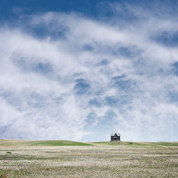 A field of grass with a small building in the middle. The sky is mostly clear with a few clouds