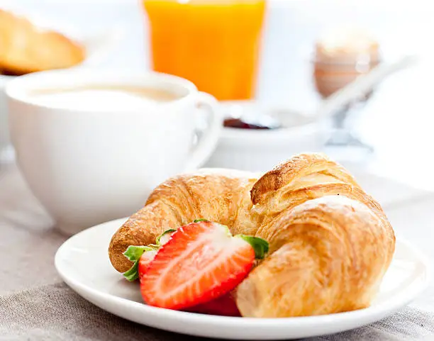 Photo of Croissant and sliced strawberry on a plate in front of mug