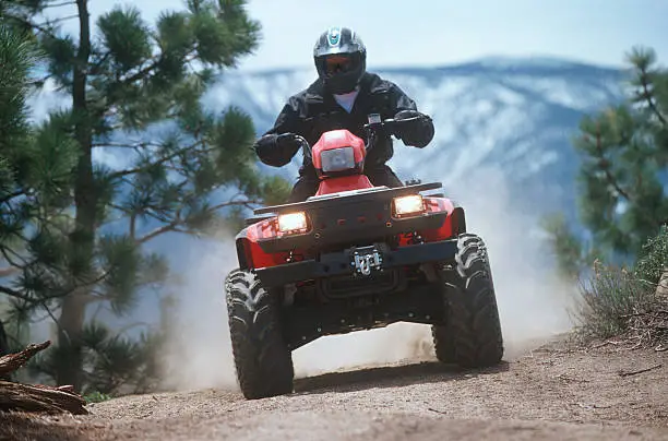 Man riding ATV on dusty mountain trail.