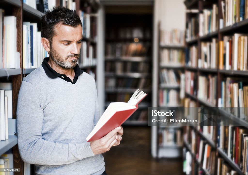 Man reading book in library isle Man reading a book in a library. Adult Stock Photo