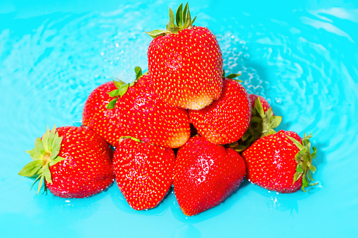 Pile of fresh, juicy strawberries partly submerged in shallow, crystal-clear blue water. Summer's sweetness essence, food-themed projects, health and wellness promotions related background.