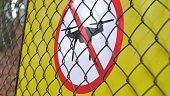 Flying Drones Prohibited Symbol on Yellow Warning Sign Behind Fence